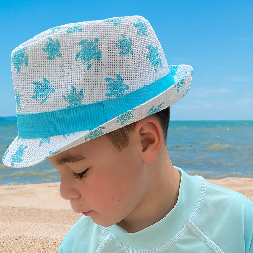 Kid on the beach wearing Flap Happy new fedora in white with aqua turtles and band