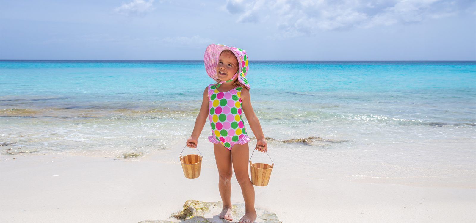 Child in a colorful swimsuit with a sun hat on a beach