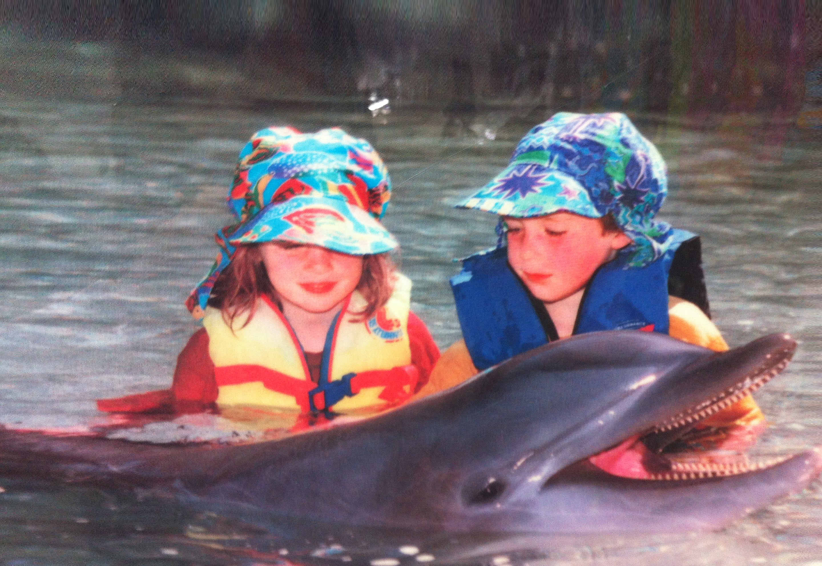 Kelly and cody in the water with a dolphin wearing Flap Happy hats