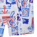Close-up of a children's zip-front garment, of a one-piece swimsuit, with a white base and a nautical print in blue, red, and light blue. The print includes an anchor, starfish, seashells, and stripes.