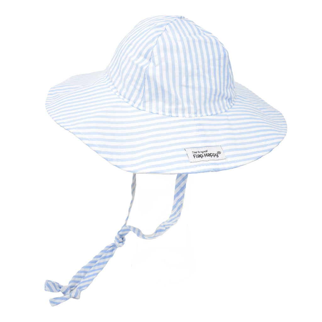 A light blue and white seersucker-striped floppy sun hat with a long, adjustable tie that extends from the sides and ties under the chin. Features a small “The Original Flap Happy” brand label on the brim.