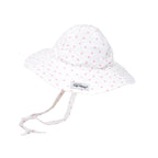 A white floppy sun hat with a small pink heart pattern, featuring a wide brim, adjustable tie that extends from the sides and ties under the chin. Features a small “The Original Flap Happy” brand label on the brim.